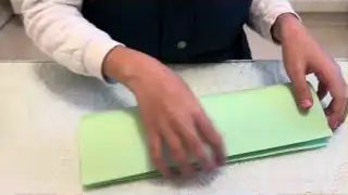 Two hands folding green paper in half