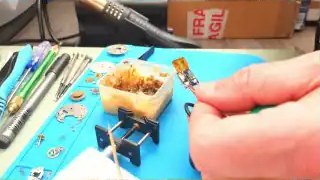 Hands near circuit board, unclear soldering setup